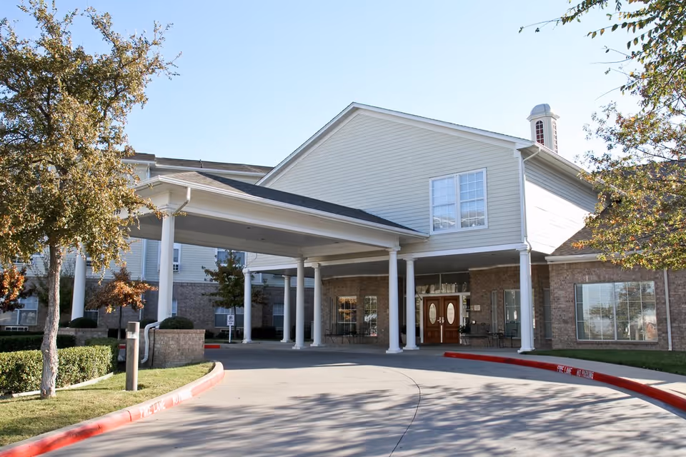 Front entrance of a two-story senior living building with a covered porte-cochère supported by white columns.