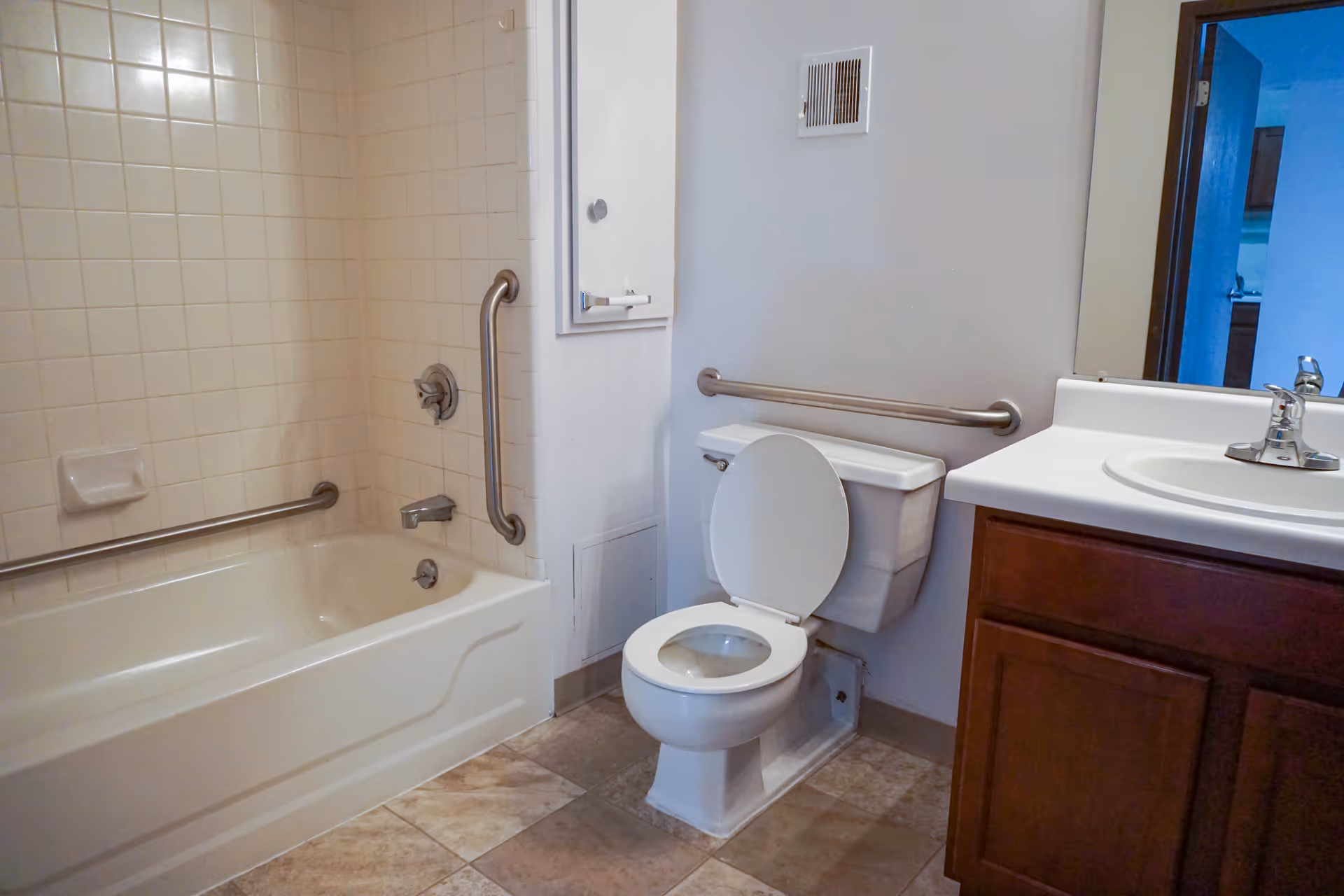 Bathroom with a tiled bathtub and grab bars, a toilet with wall-mounted grab bar, and a sink with vanity.