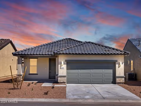 Single-story house façade with a two-car garage, desert landscaping, and a colorful sunset sky.