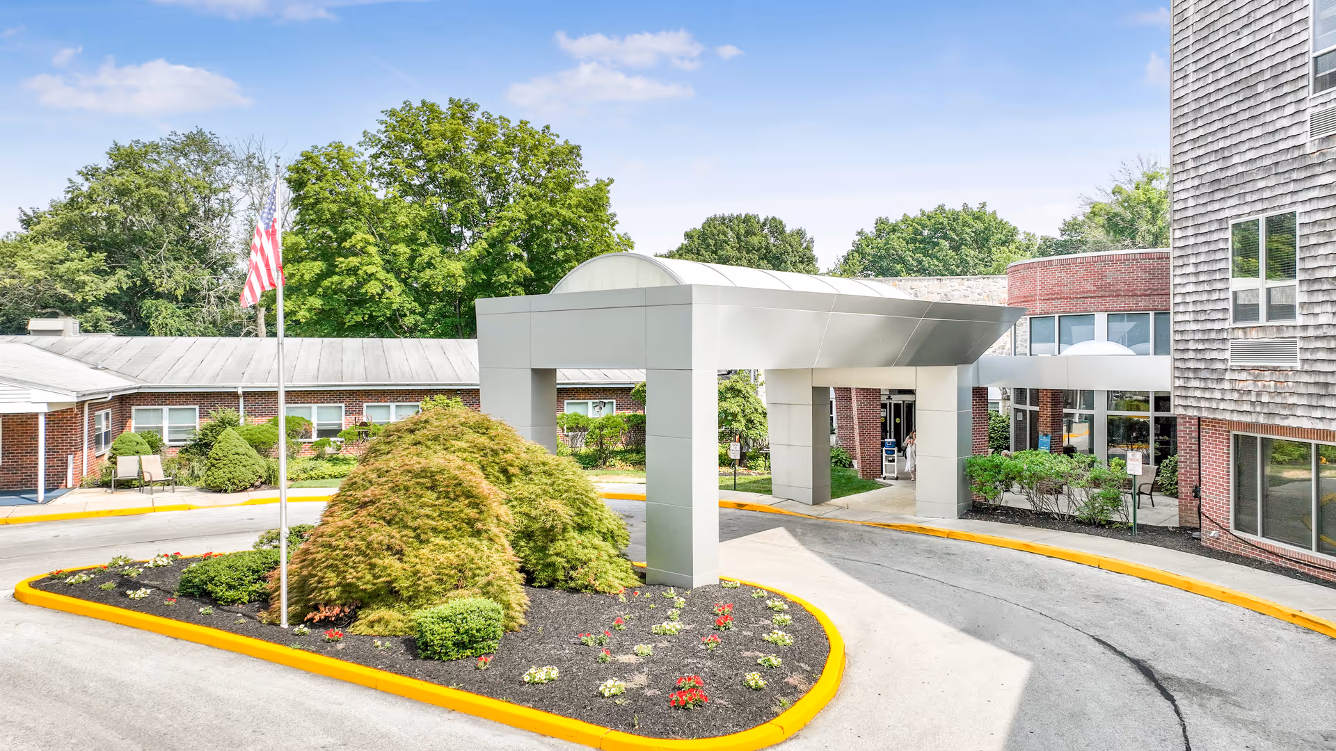 Front entrance of Springfield Crossings showing a covered drop-off canopy, landscaped island, and an American flag.