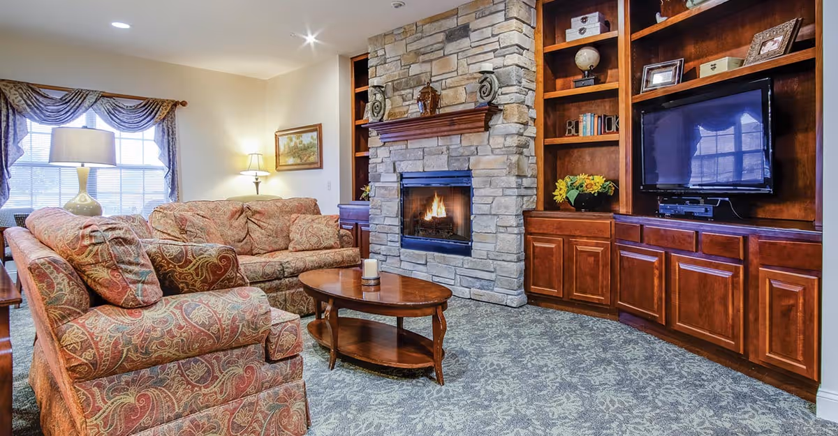 Cozy living room with patterned sofas, a wooden coffee table, a stone fireplace and built-in wooden shelving with a TV.