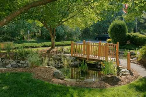 A wooden pedestrian bridge spans a small pond in a landscaped garden.