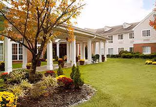 Front exterior view of Brighton Gardens of Edison with manicured lawn, trees, and walkway.
