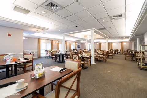 Bright, spacious dining room with multiple set tables and chairs, decorative columns, and service carts.