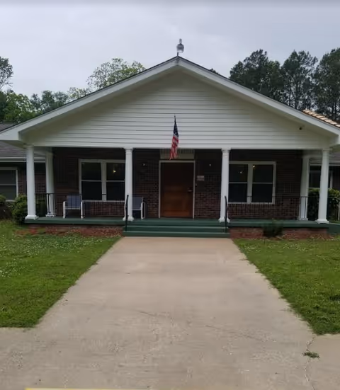 Front view of a single-story brick facility with white columns and a flag.