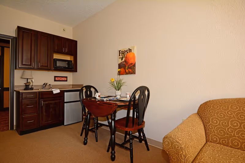 Small apartment-style living area with a kitchenette, a round dining table with two chairs, and a patterned sofa.