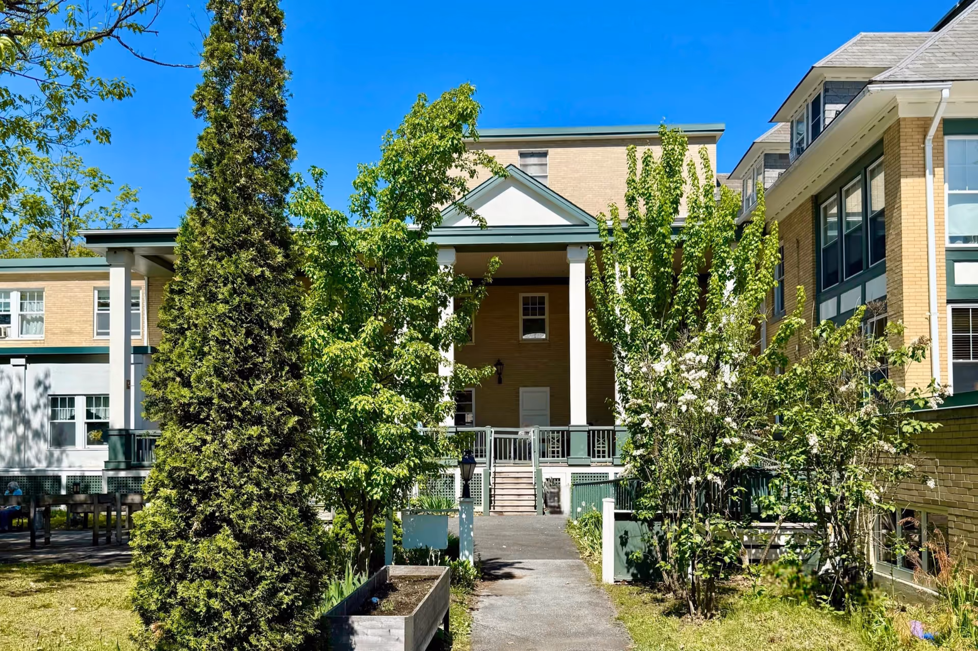 Exterior view of Heaton Woods Residence showing a brick building entrance with white columns and surrounding trees.