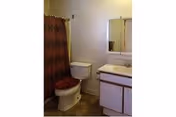 Small bathroom with a toilet, patterned shower curtain, vanity with sink and mirrored medicine cabinet, and tiled floor.