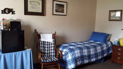 Bedroom with a blue plaid bedspread, wooden chair, and dresser against wall.