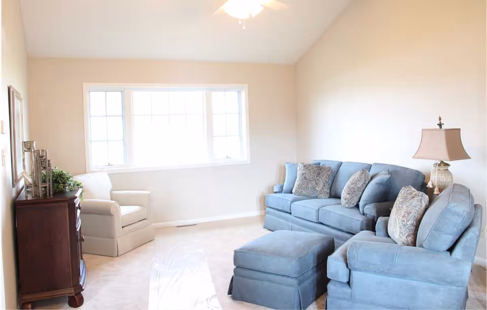 Bright living room with a blue sofa set, ottoman, an armchair, side table and a large window.