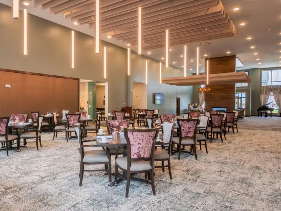Spacious senior living dining room with multiple tables and upholstered chairs under modern hanging pendant lights.