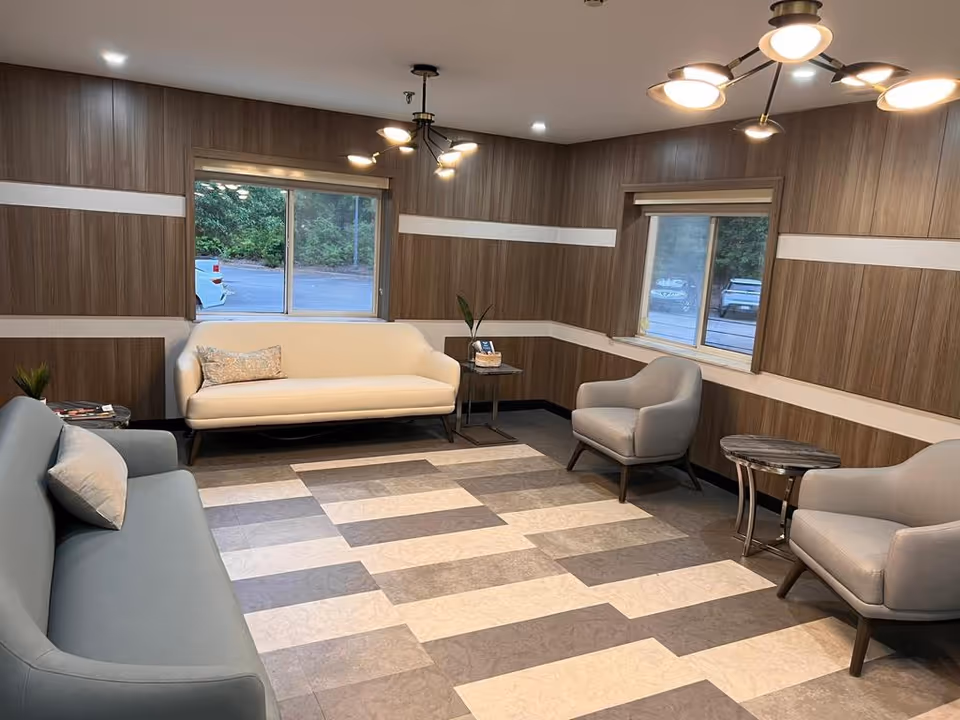 Modern lounge with sofas, armchairs, side tables, and large windows in a wood-paneled room.