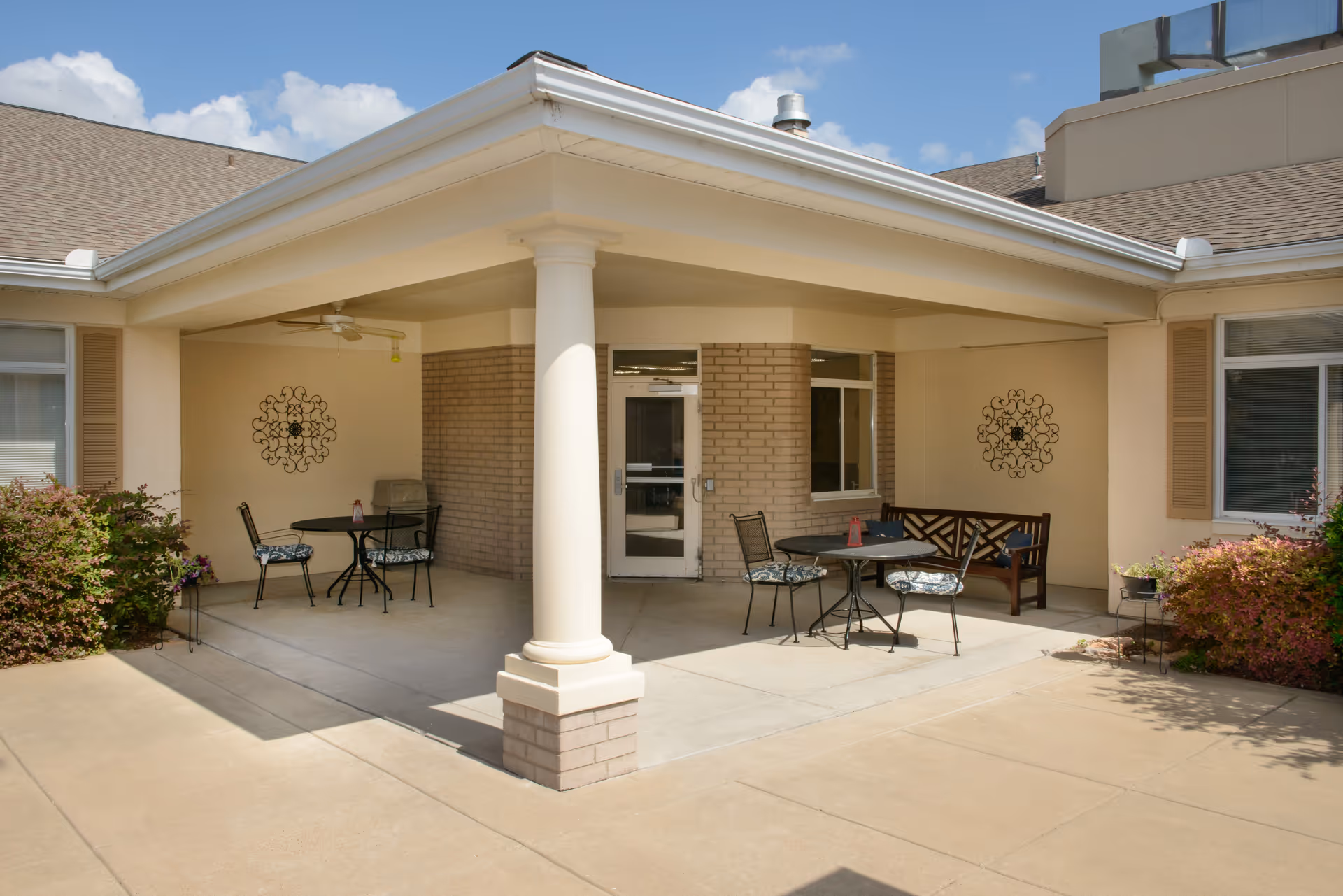 Covered courtyard patio with a central column, round tables, chairs and a bench outside the building entrance.