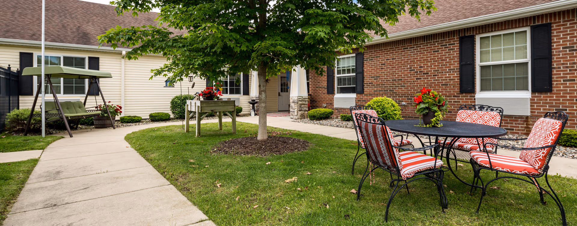 Outdoor courtyard with a round table and red-cushioned chairs, a swing, and a brick building facade.