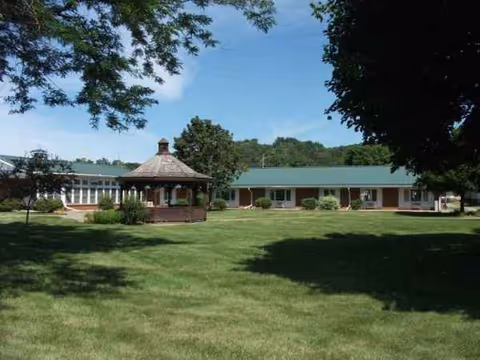 Single-story care facility building with a green roof, gazebo, and expansive grassy lawn.