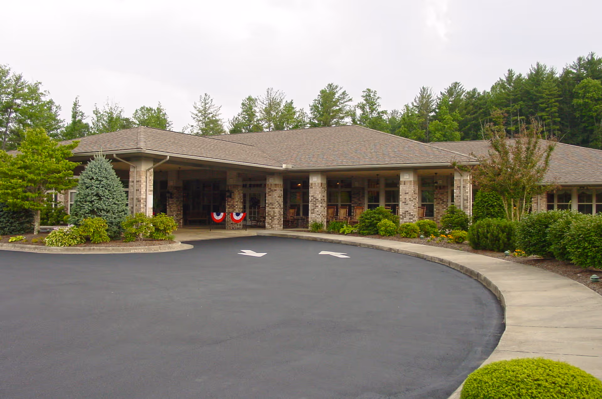 Single-story brick senior living building with a covered entrance, circular driveway and landscaped shrubs.