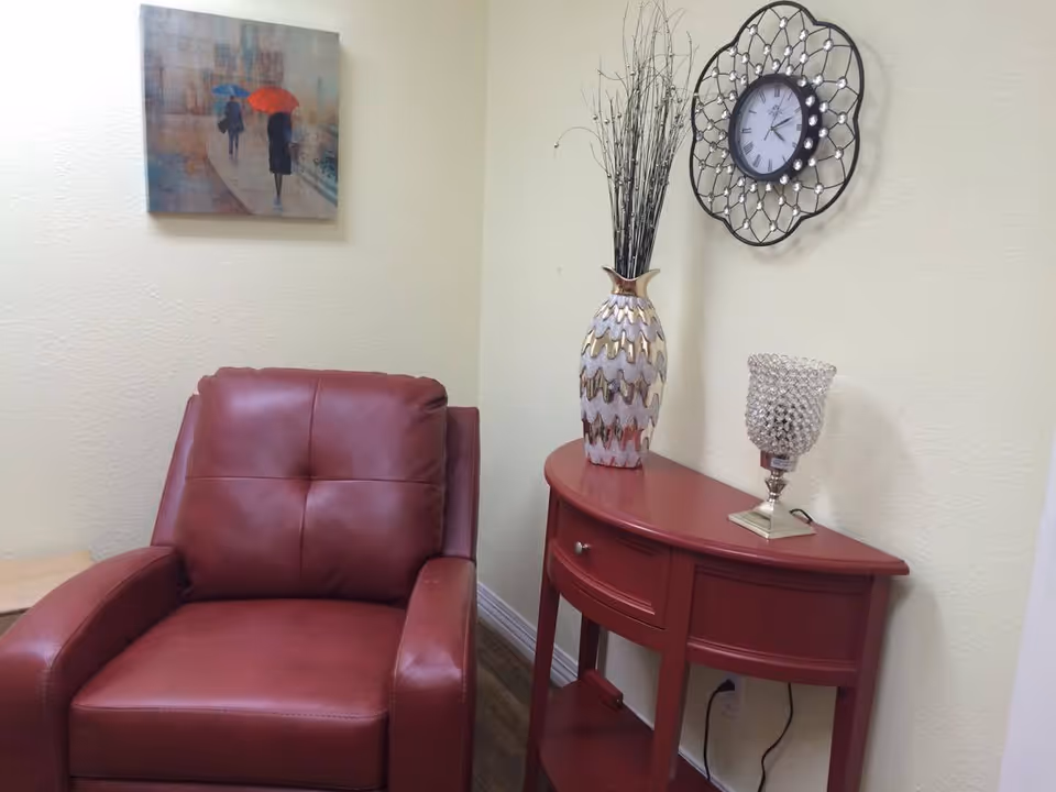 Red leather armchair next to a red half-moon console table with a decorative vase, crystal lamp, wall clock, and a painting on a pale yellow wall.