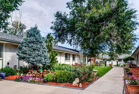 A courtyard path with flowering plants and trees along single-story building facades.