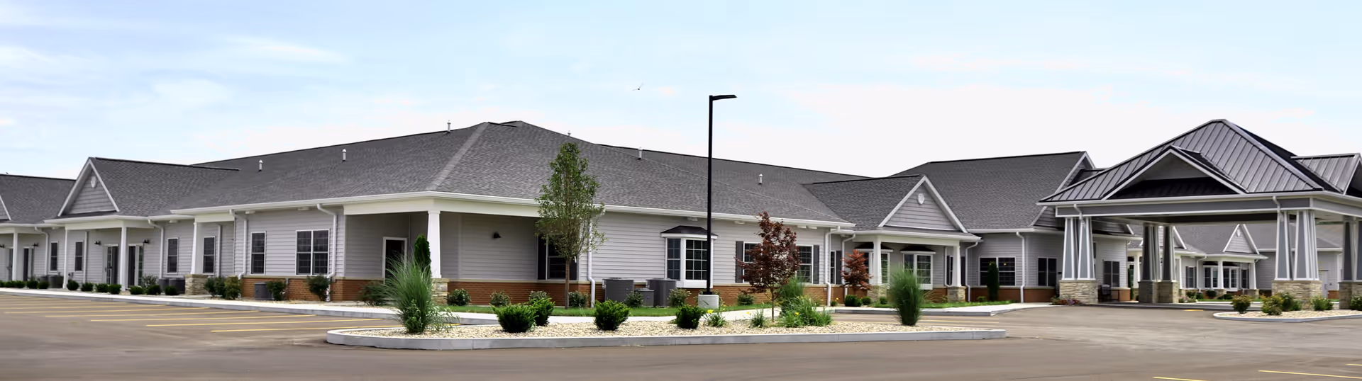 Front exterior of Liberty Village of Jerseyville senior living building with a covered entrance, parking area, and landscaped islands.