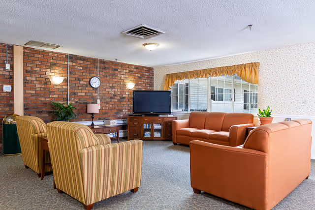 A cozy common living room with sofas and armchairs facing a TV set against a brick accent wall.
