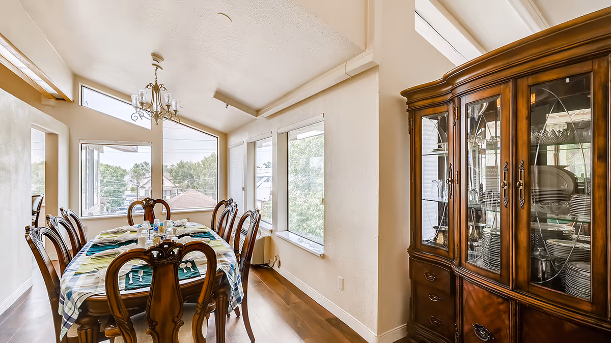 Dining room with a wooden table set for a meal, high windows, chandelier, and a large china cabinet.