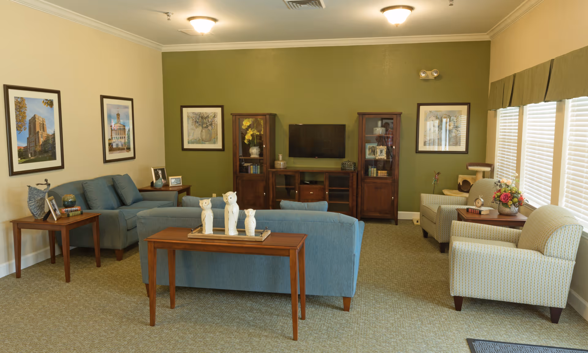 Comfortable senior living common room with sofas, armchairs, a TV cabinet and framed artwork.