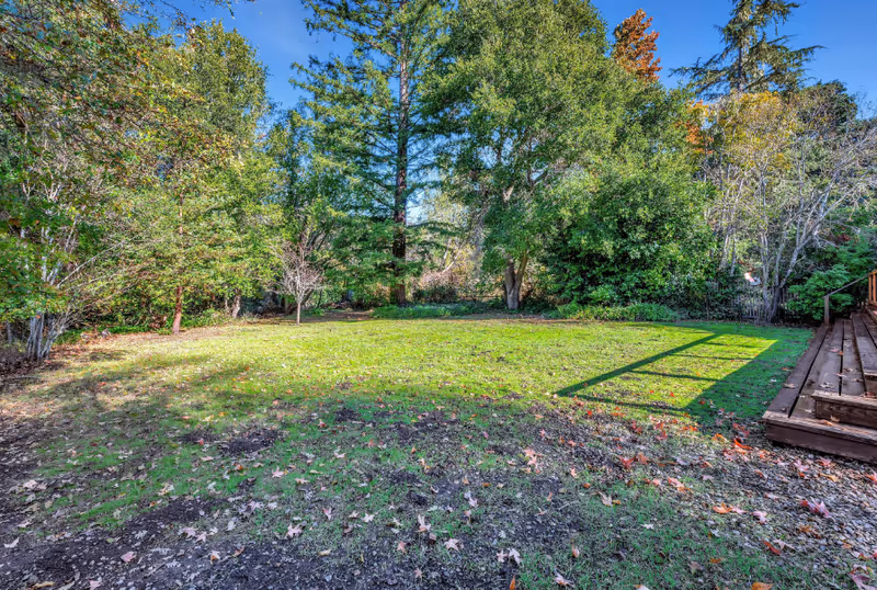 Meadow Creek Senior Living outdoor yard with trees, grass, and a wooden deck on the right.