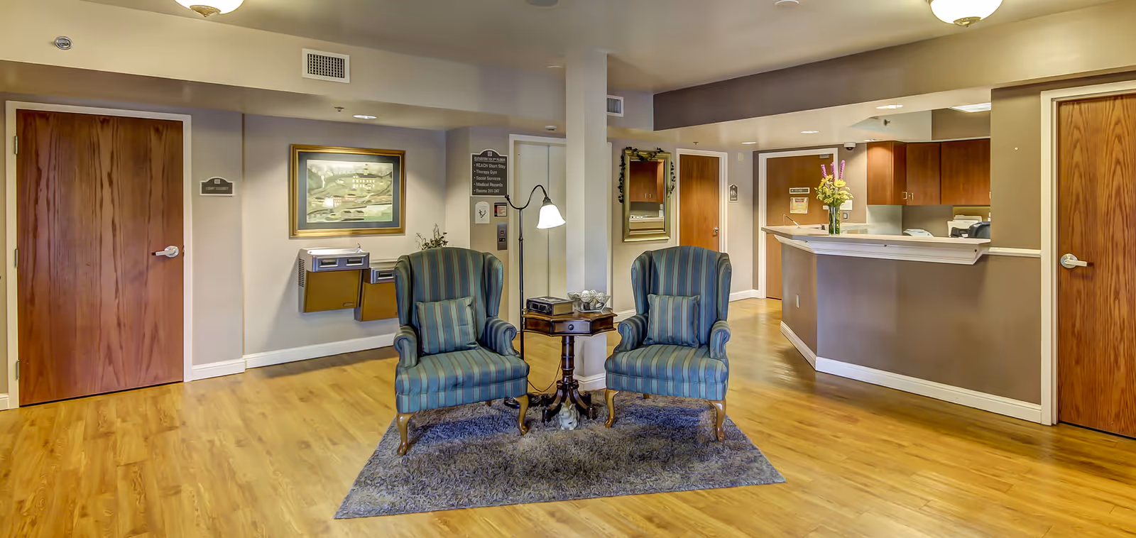 A reception-style common area with two upholstered armchairs on a rug around a small side table and a reception desk in the background.