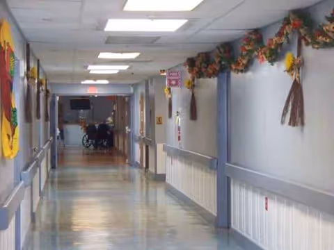 Long well-lit corridor in a senior care facility with garlands and a distant wheelchair.