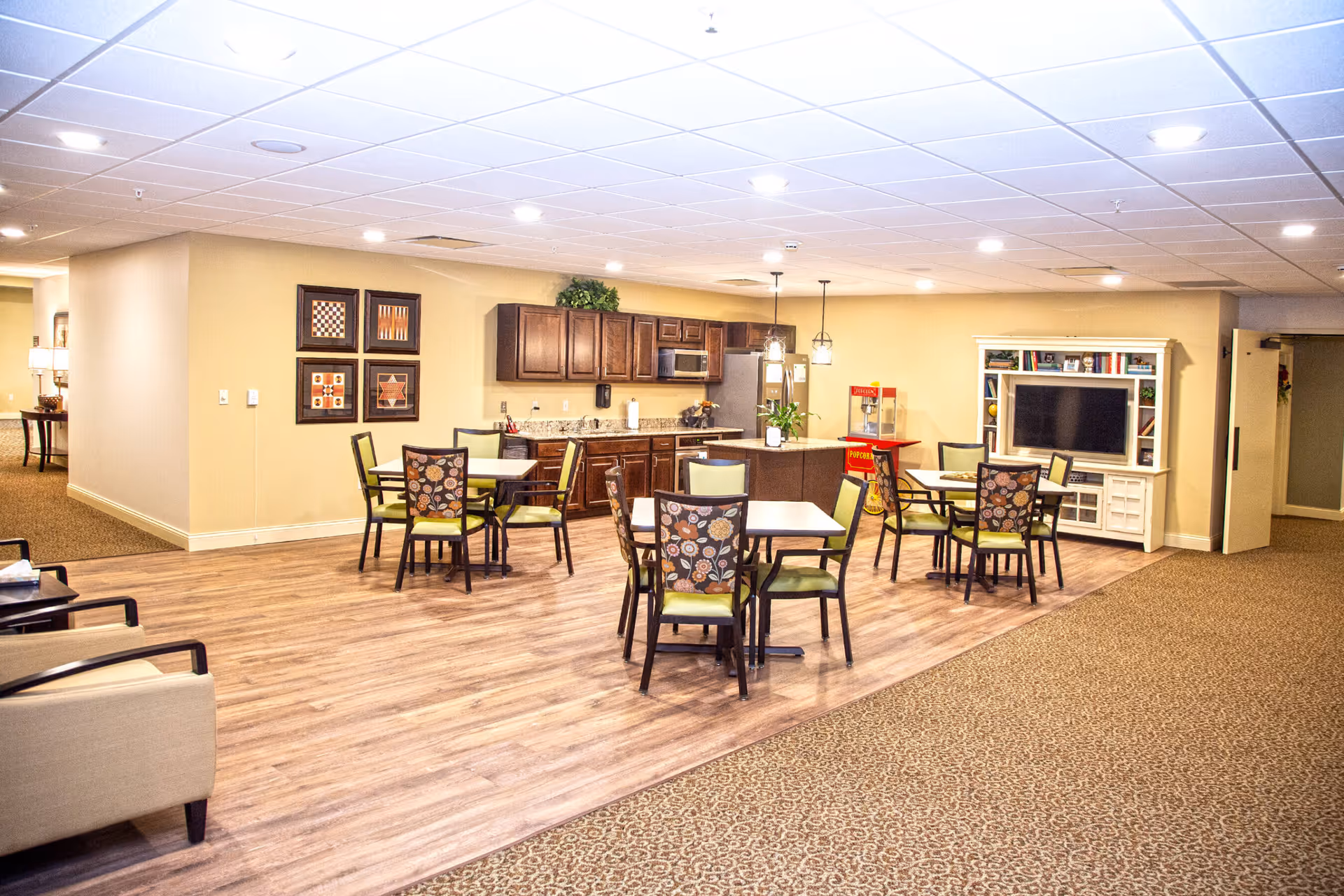 Open common dining and lounge area with tables and chairs, a kitchenette and a TV entertainment center.
