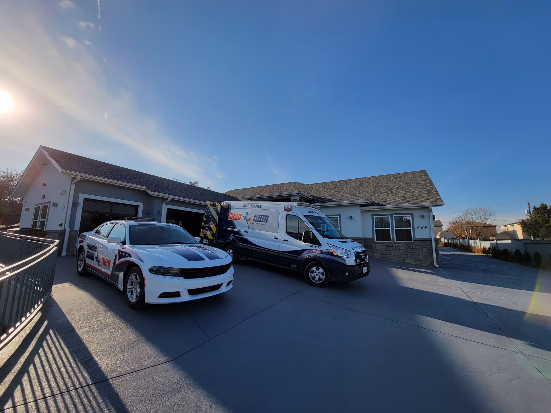 Exterior view of a single-story building with a driveway where a white police car and an ambulance are parked under a clear blue sky.