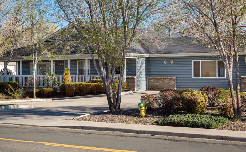 Blue, single-story building exterior labeled The Verandas Assisted Living with trees and shrubs.