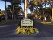 Entrance sign for Palms of Manasota surrounded by palm trees and landscaping.