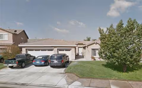 Front view of a single-story home with a two-car garage and a large tree.