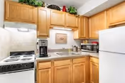 Small kitchen with wooden cabinets, a white electric stove, a coffee maker, a microwave, a white refrigerator, and decorative items on top of the cabinets.