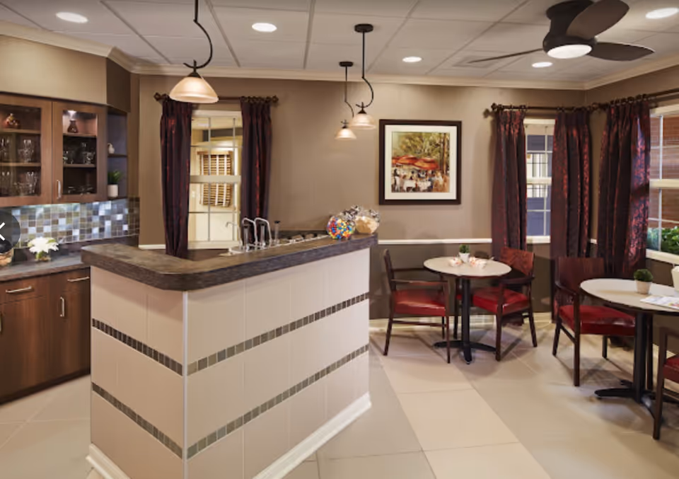 Cozy communal dining area with a service counter/kitchenette, round tables and red chairs under pendant lights.