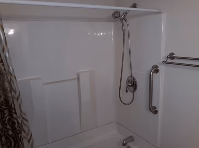 White bathtub and shower stall with a handheld showerhead, grab bar, towel rack, and patterned shower curtain.