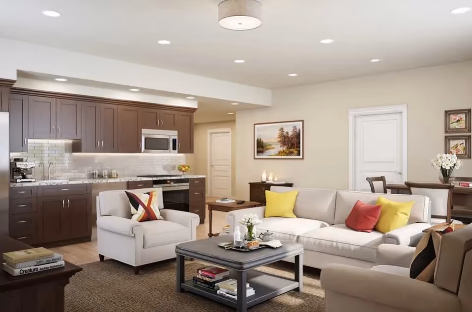 Open-concept living area featuring a beige sofa and armchair with colorful pillows, a coffee table, and a kitchen with dark wood cabinets.