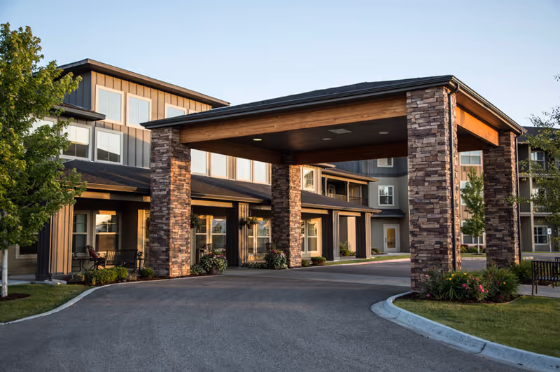 Front entrance of a senior living building with a covered porte-cochere supported by stone columns.