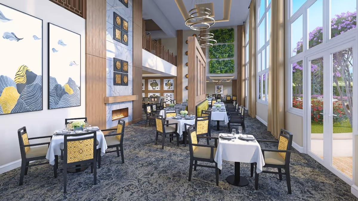 Spacious senior living dining room with set tables, high ceilings, a fireplace, and floor-to-ceiling windows overlooking a garden.