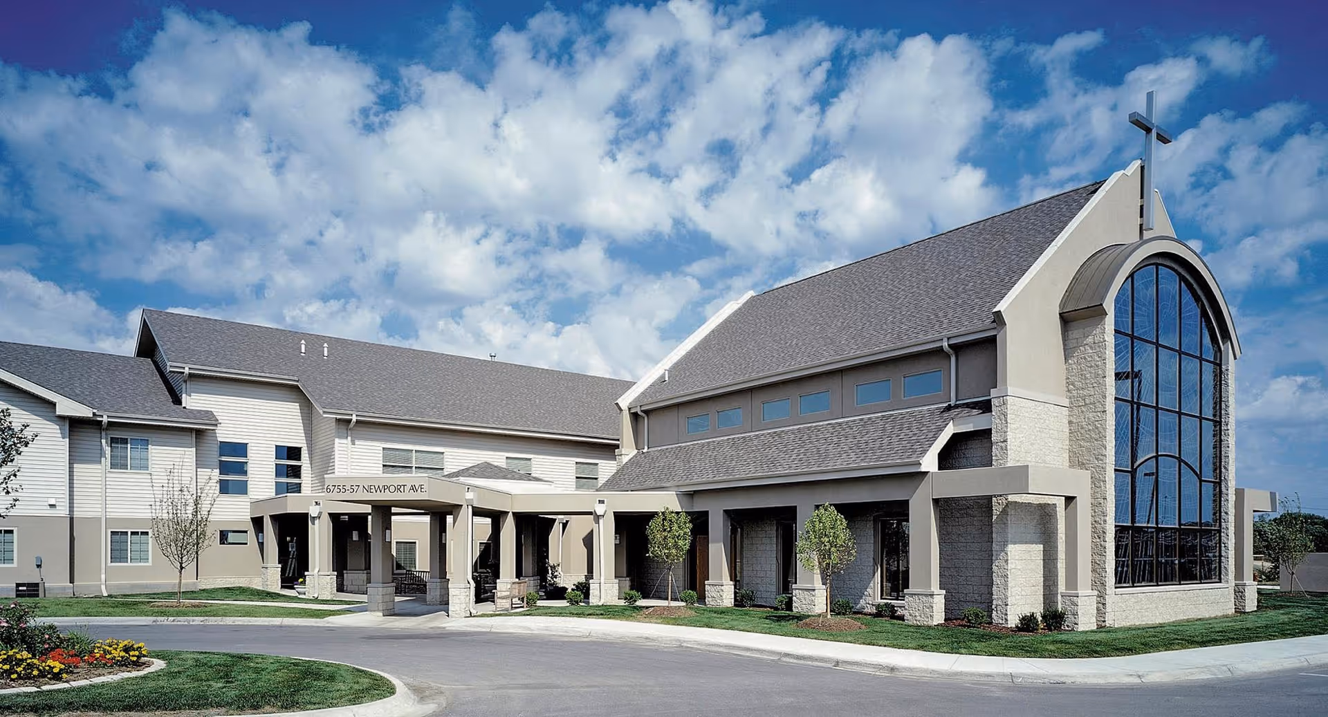 Front exterior of Immanuel Courtyard senior living facility with a covered entrance, landscaped grounds, and a large arched window topped by a cross.