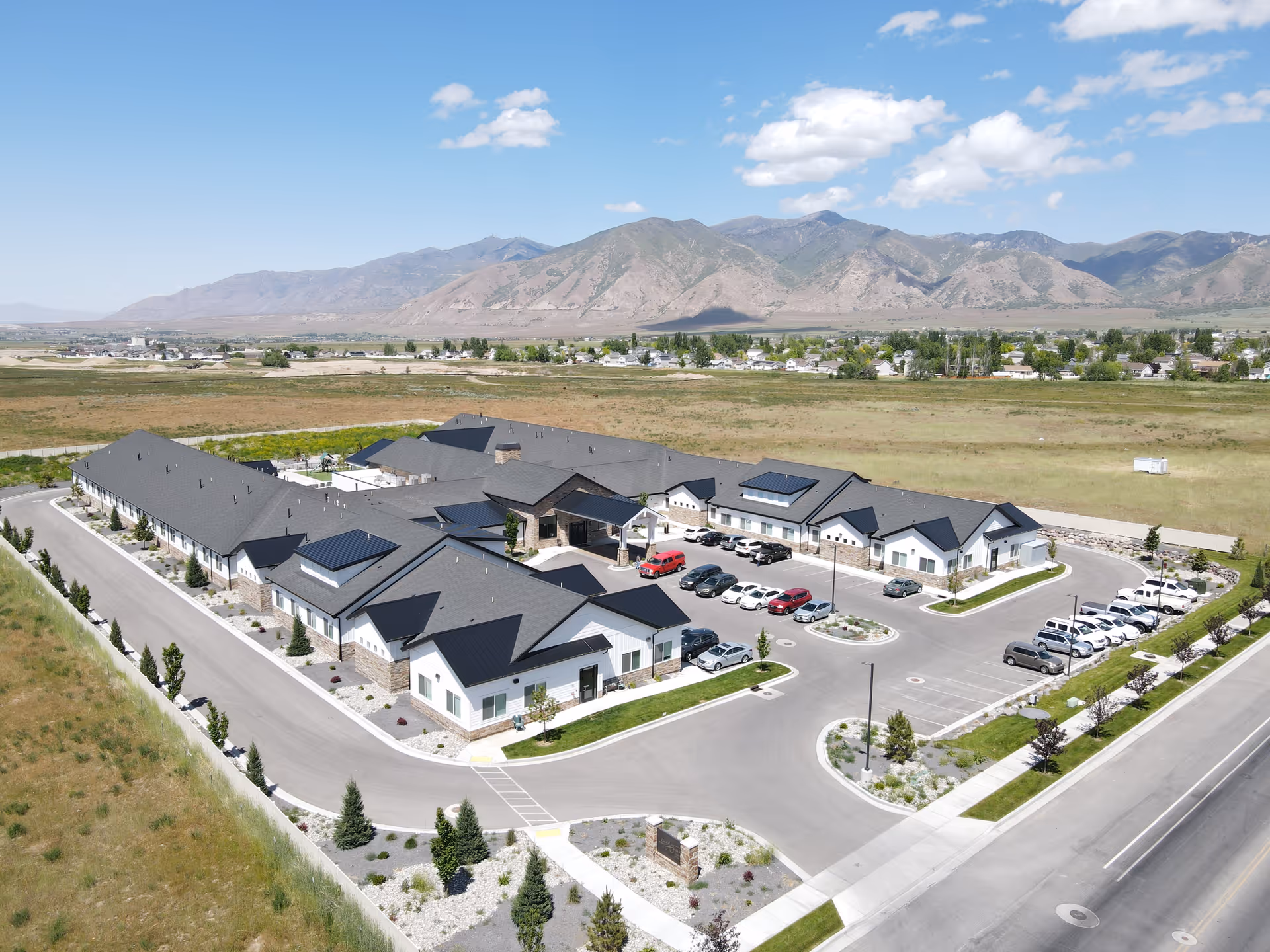 Aerial view of a single-story assisted living complex with parking lots, landscaped grounds, and mountains in the background.
