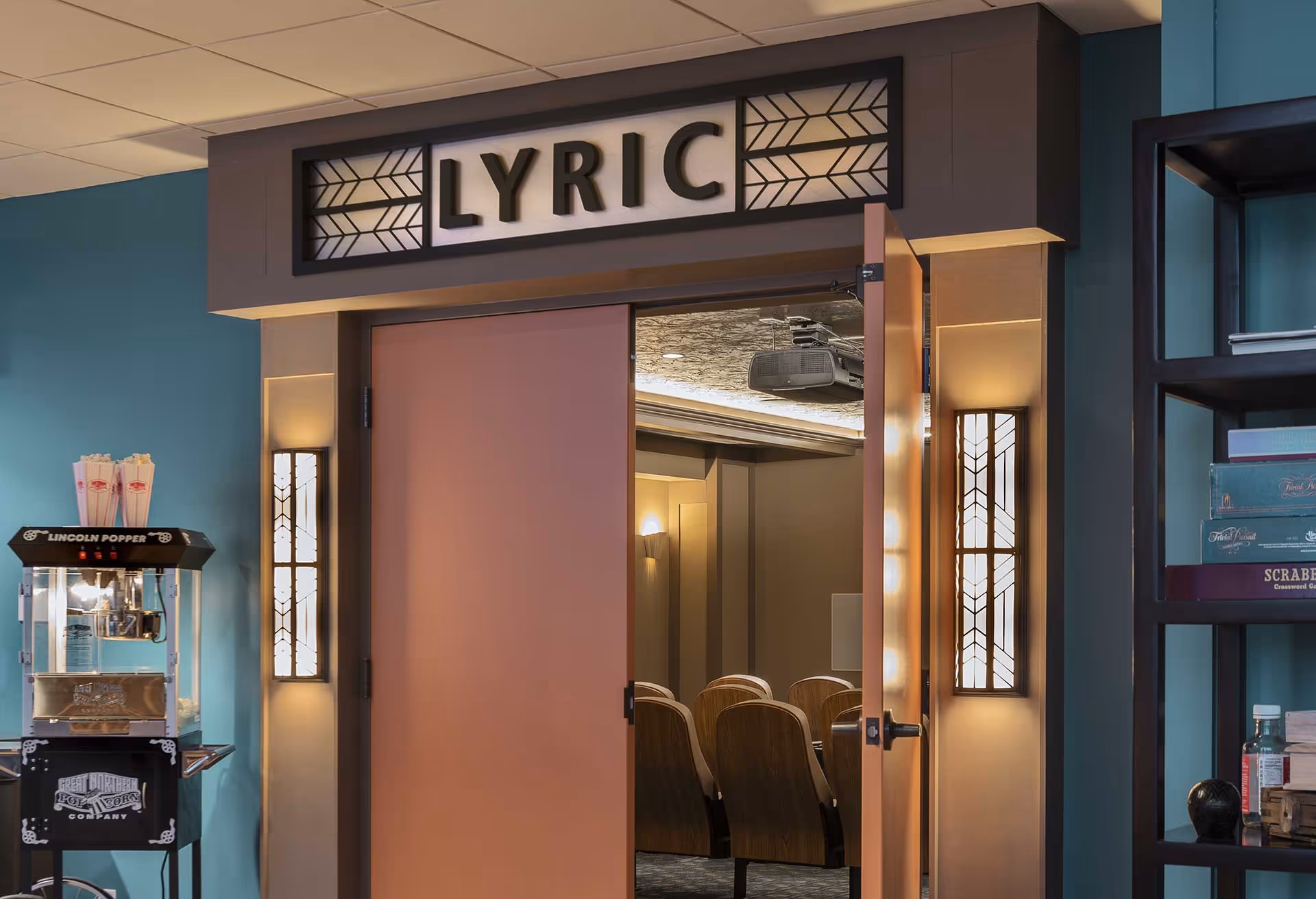 Entrance to a small theater labeled "LYRIC" with open double doors showing rows of seats, a popcorn machine to the left, and shelving to the right.