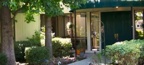 Exterior view of Greenhaven Place entrance with glass doors, trees, and landscaped shrubs.