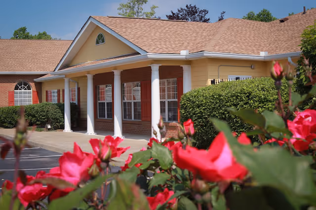 A view of the exterior of Belvedere Commons of Franklin, featuring a yellow building with white columns, red shutters, and blooming pink flowers in the foreground.