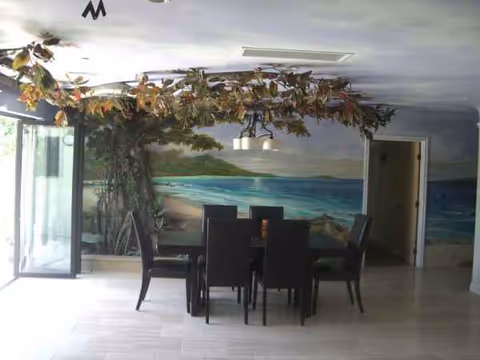 Interior dining room with dark table and chairs, ocean mural, and hanging leaf decor.