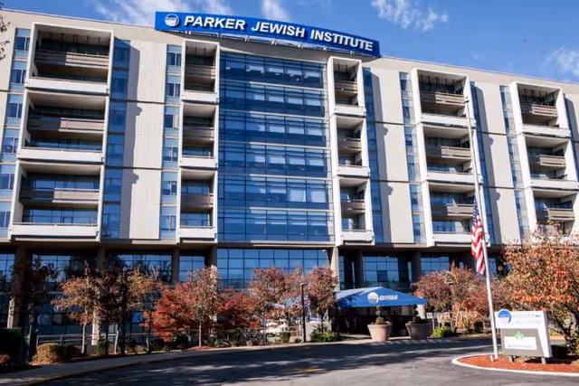 Front view of Parker Jewish Institute building with entrance, trees, and American flag.