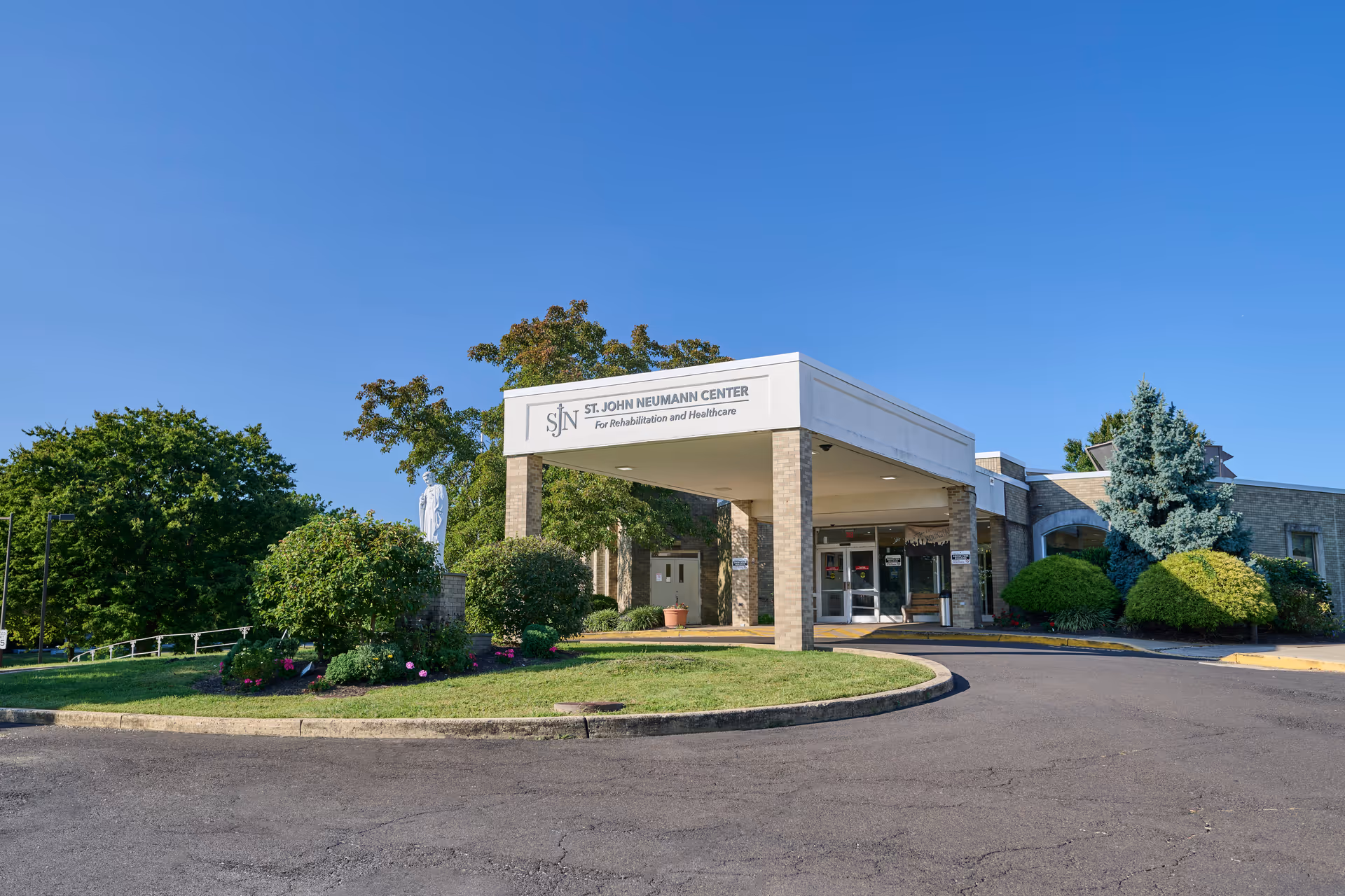 Front entrance of the St. John Neumann Center for Rehabilitation & Healthcare with a covered drive-through and landscaped grounds.