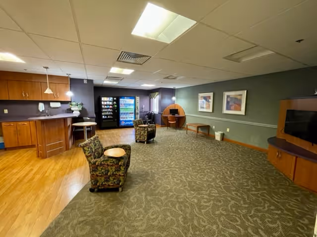 Community lounge area with armchairs, a kitchenette, vending machines, and a TV.