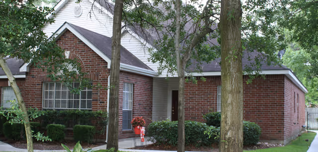 Brick senior living facility exterior with trees, shrubs, and a small entrance path.